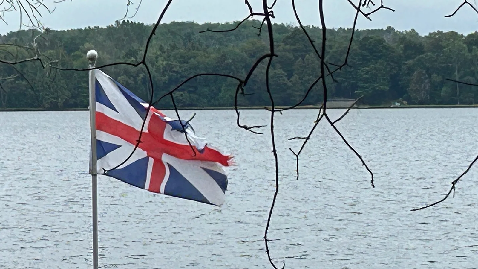 Torn Union Jack flag flying by lake shore